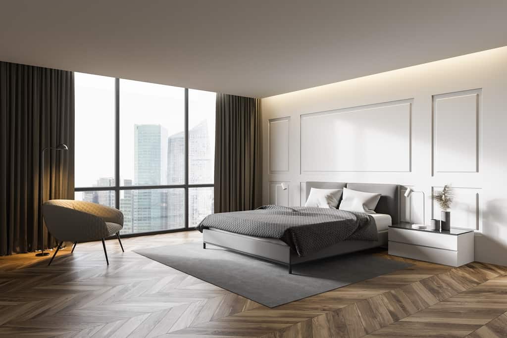 bedroom interior with white walls, wooden floor, rug under the bed and armchair