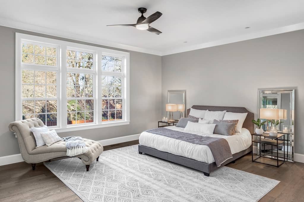 master bedroom with large windows, rug under the bed and a bench, additional furniture